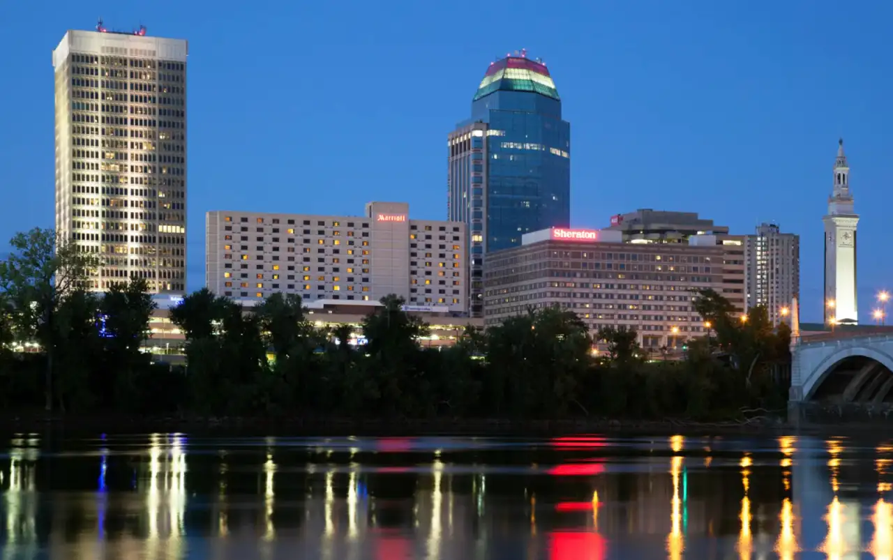 Downtown Springfield, Massachusetts at dusk over the Connecticut River — the glass Monarch Place tower, the Marriott and Sheraton hotels, and the Campanile clock tower, with the Memorial Bridge crossing at right