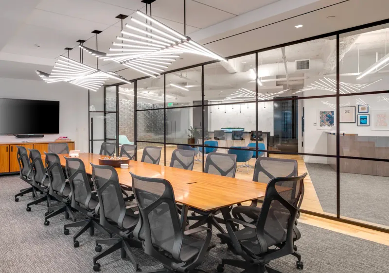 Corporate conference room with a finished drywall ceiling and cove lighting, a glass partition wall, and a wall-mounted display